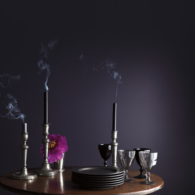 A wooden table with glasses, dishes, and candles in front of a dark purple wall.
