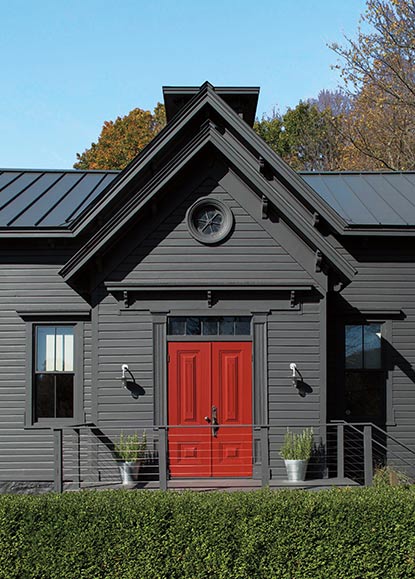 A dark gray-painted house with a bright red front door, a front hedge and autumn foliage.