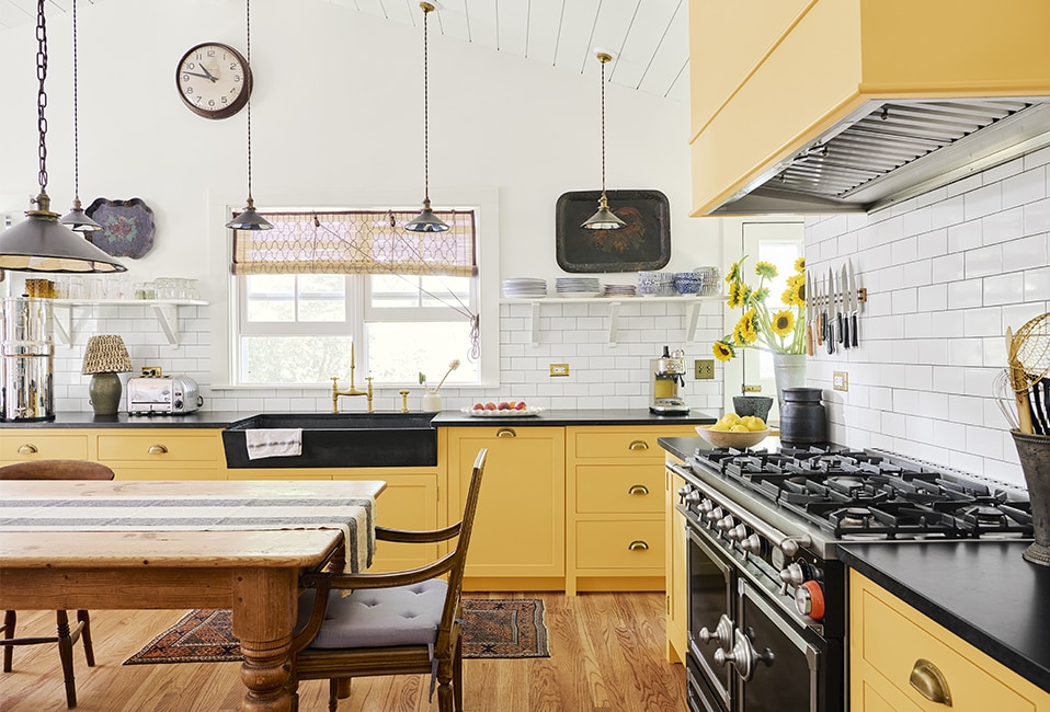 Яркая, веселая кухня с белыми стенами и шкафами, выкрашенными в желтый цвет, деревянным столом и деревянным полом.