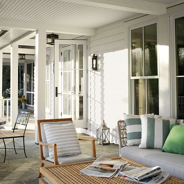 Terrasse couverte blanche avec plancher de béton et plusieurs endroits pour s’asseoir.