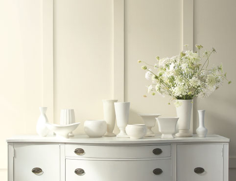A warm white painted wall creates a soft backdrop for vases and flowers atop a traditional console. A warm white painted wall creates a soft backdrop for vases and flowers atop a traditional console.