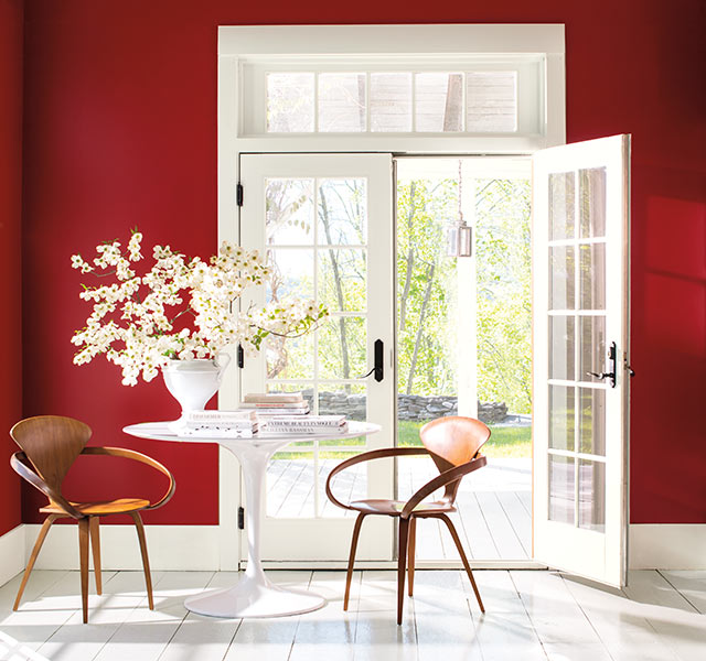 A rich red sitting room is flooded with light through several white French doors. 
