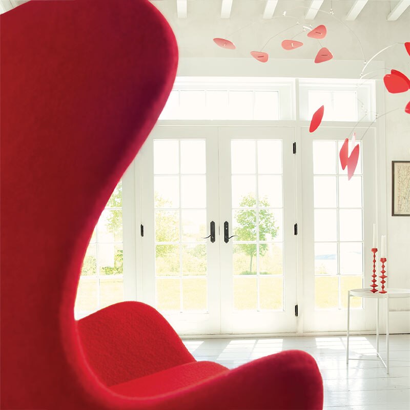 A red tulip chair faces a white room featuring a red mobile and French doors with views to greenery outside.