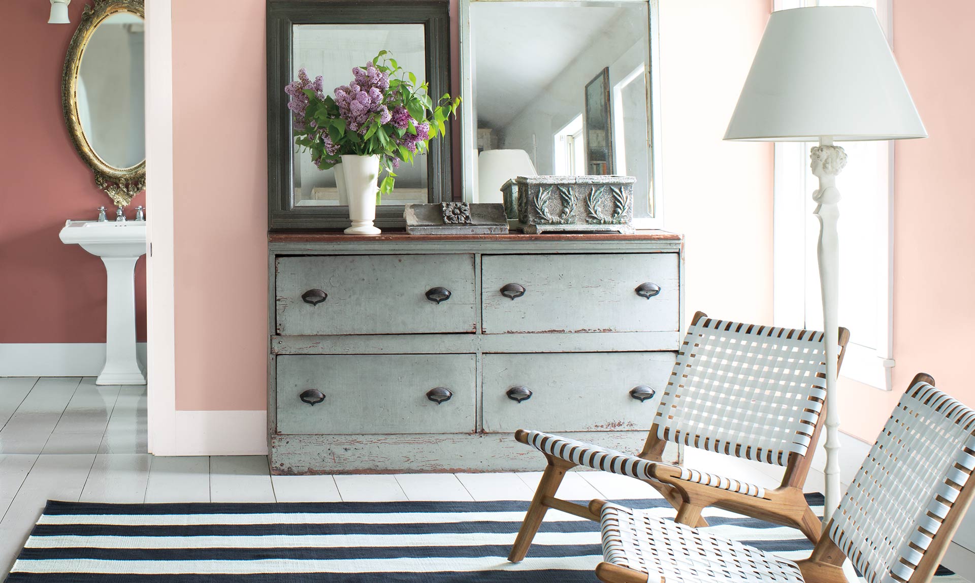 A pink-hued bedroom with angled ceiling and grey bureau features a a seating area with two contemporary chairs and a glimpse into the powder room A pink-hued bedroom with angled ceiling and grey bureau features a a seating area with two contemporary chairs and a glimpse into the powder room