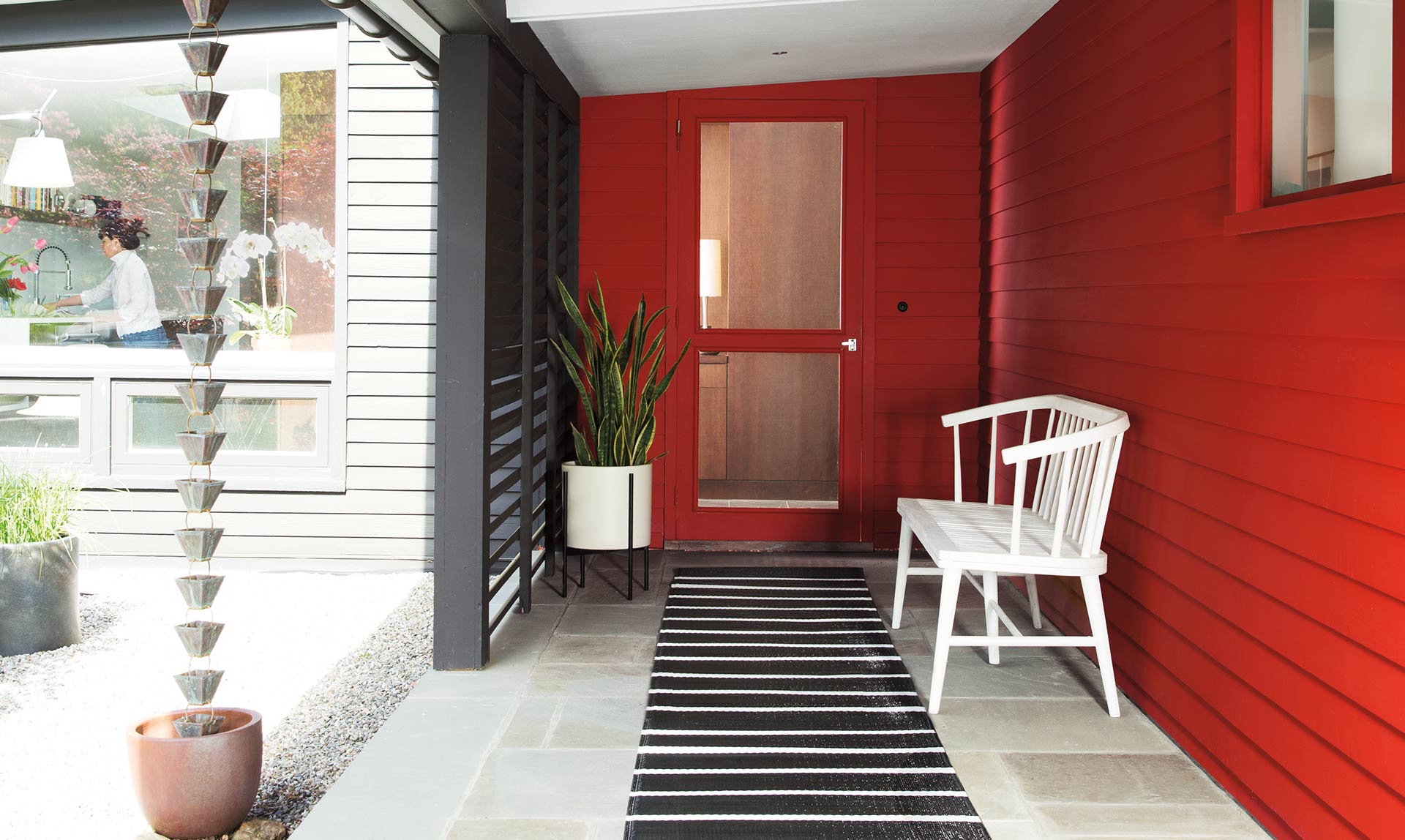 A semi-enclosed entryway with white wood bench against red shingled wall.