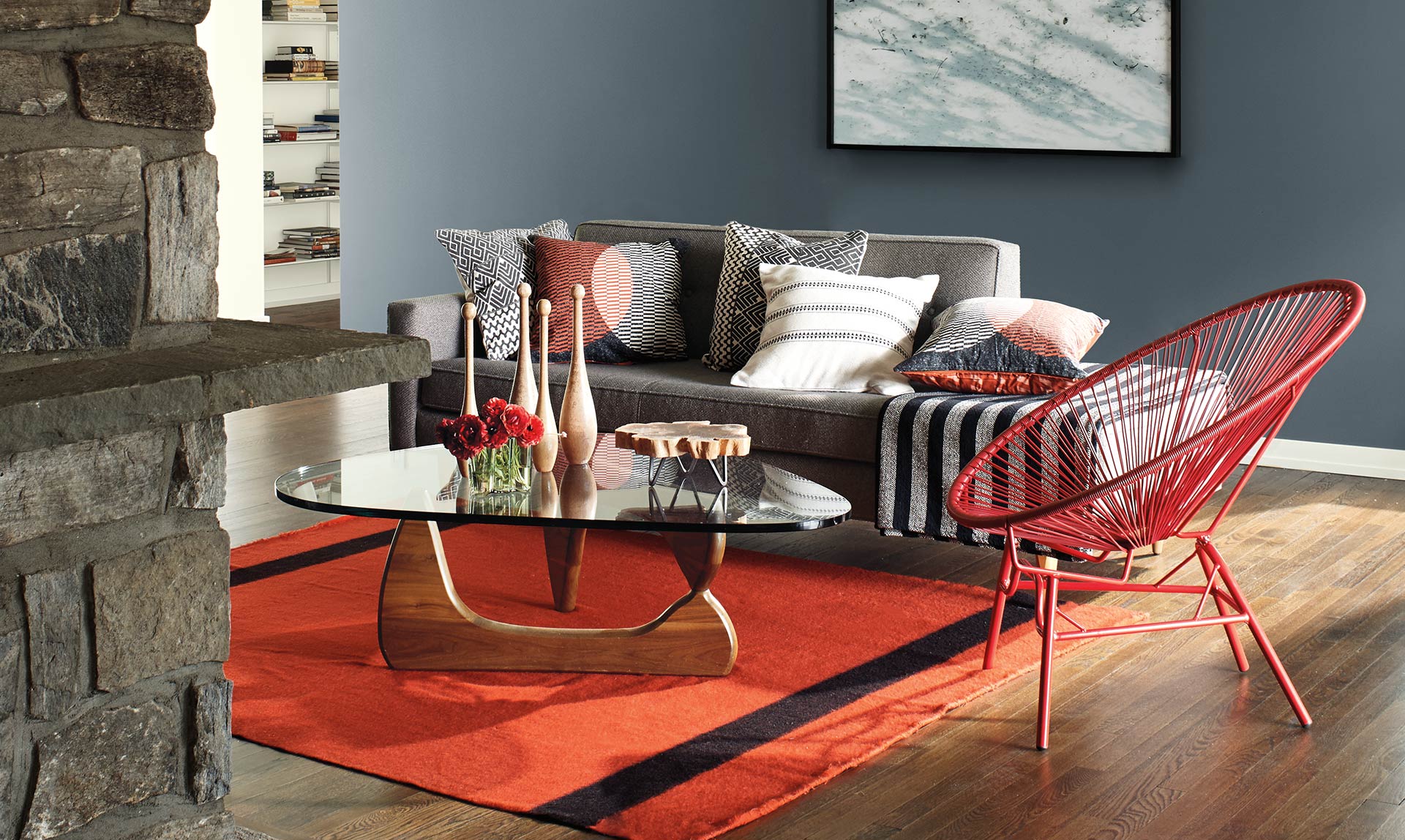 An intimate living room with gray accent wall, stone mantle, wood floors and red area rug is equal parts contemporary and cozy.