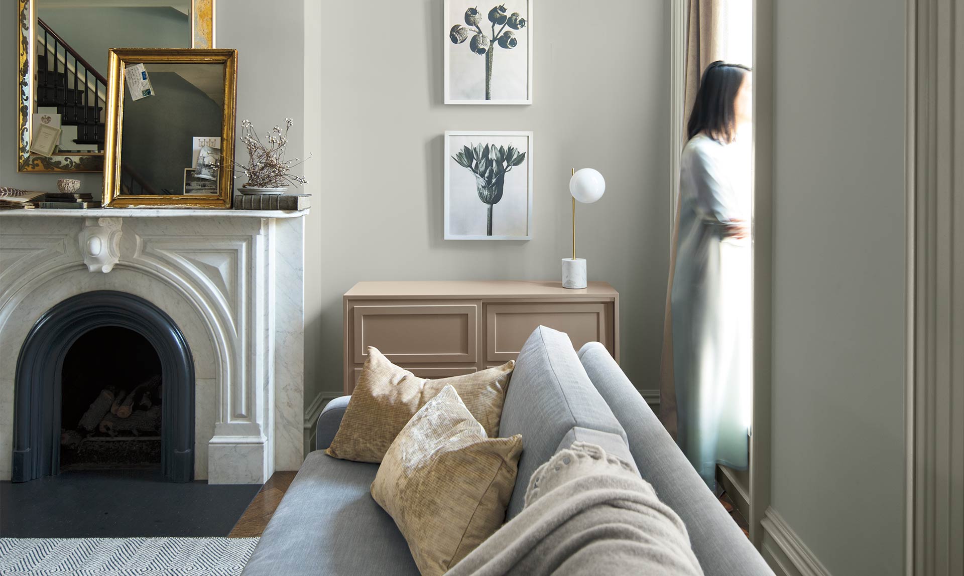 In a gray-painted living room a woman looks out the window. Colour of the Year 2019