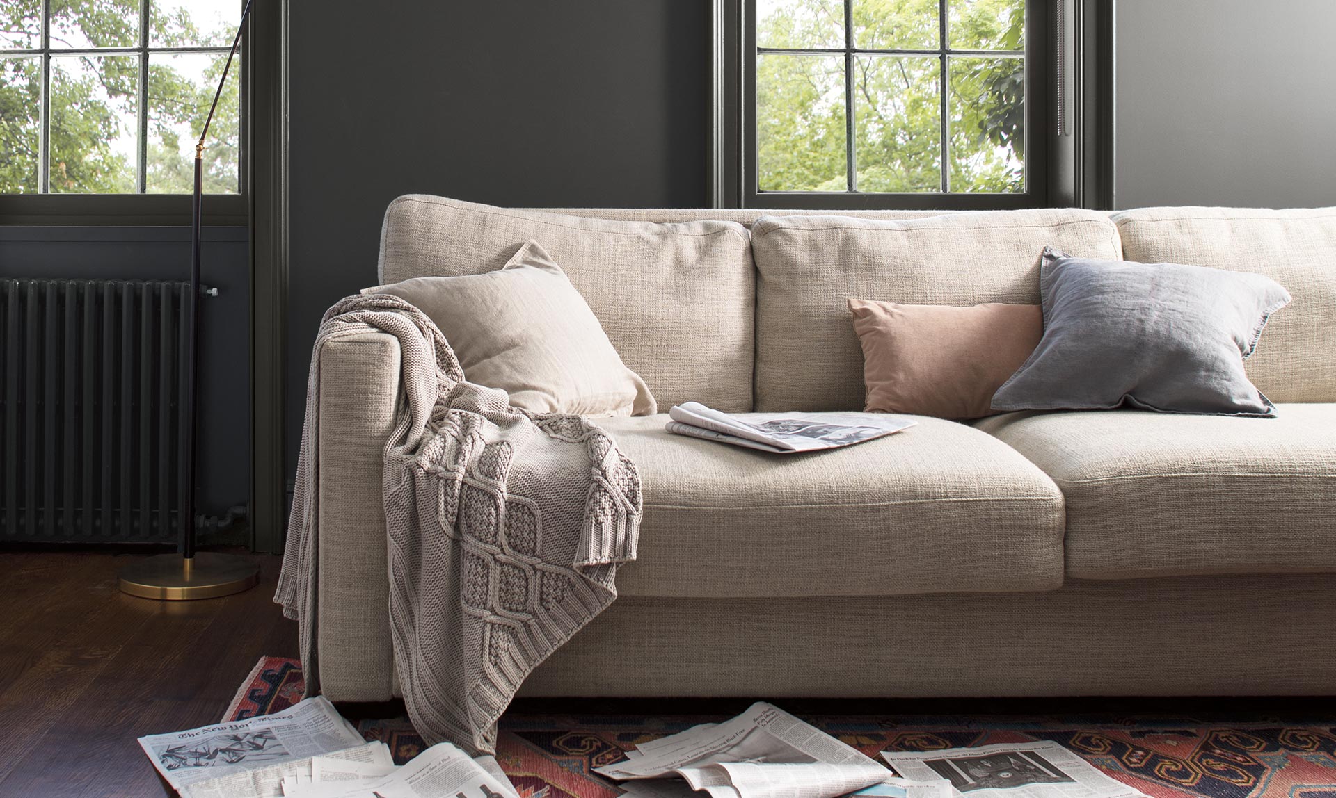 Charcoal gray-painted walls, trim and windows add depth to a cozy family room with beige couch. Colour of the Year 2019