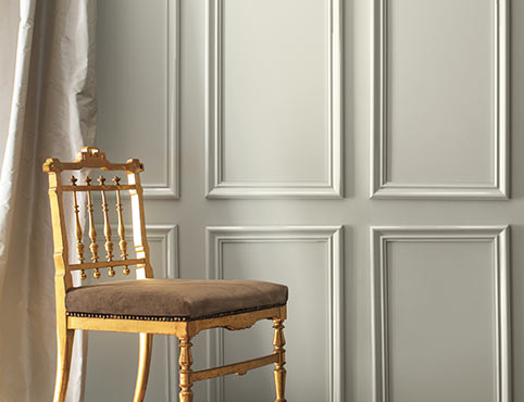 A wall painted in Metropolitan AF-690, a cool gray, cream-coloured silk curtains, and a formal gold chair.