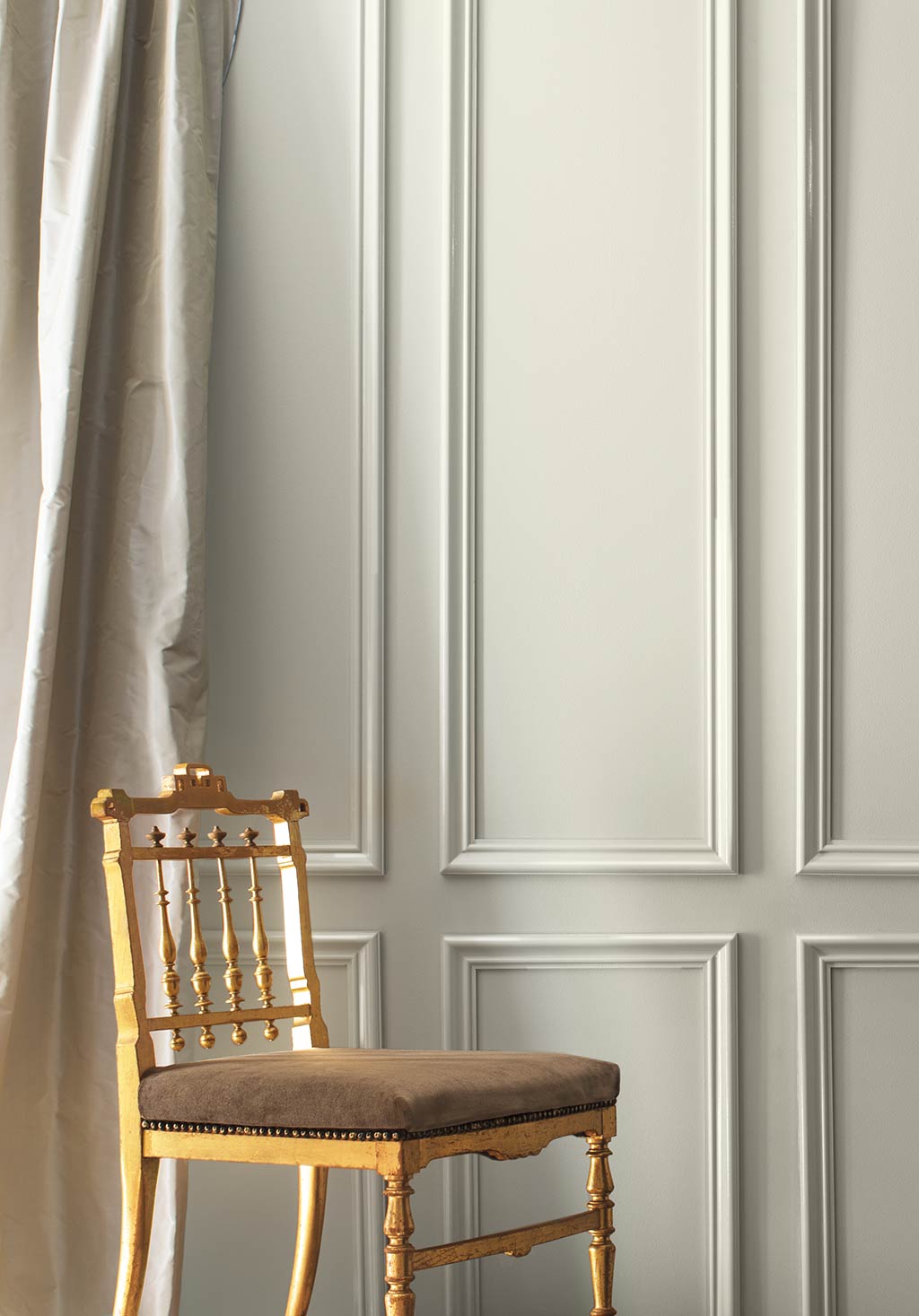 A gray-painted wall and cream-coloured silk curtains frame a formal gold chair. Colour of the Year 2019