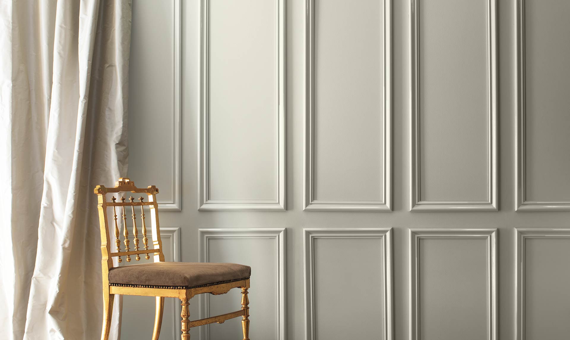 A gray-painted wall and cream-coloured silk curtains frame a formal gold chair. Colour of the Year 2019