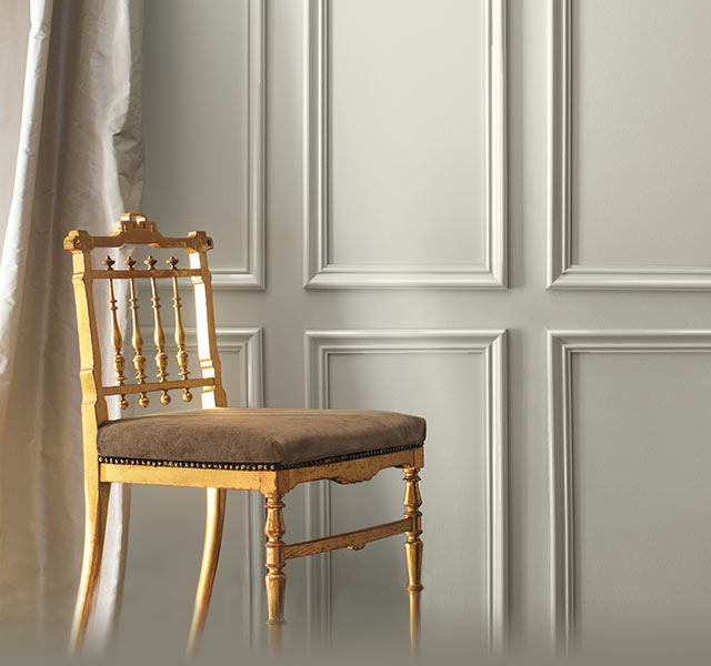 A gray-painted wall and cream-coloured silk curtains frame a formal gold chair. Colour of the Year 2019