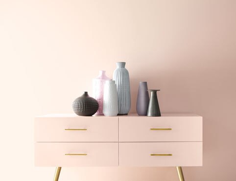 A wall painted in First Light 2102-70, a soft pink, a pink console with gold handles and multiple vases.
