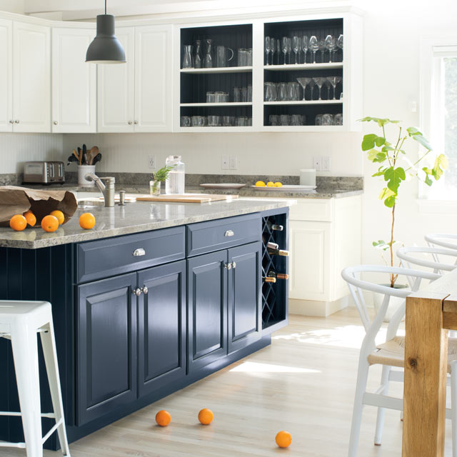 Une cuisine claire et aérée présente un îlot bleu et des murs et armoires blancs