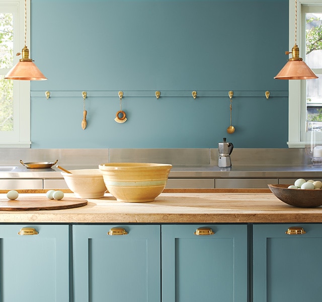 A kitchen with walls and cabinets painted in warm blue Aegean Teal 2136-40 and bowls on a butcher block countertop.