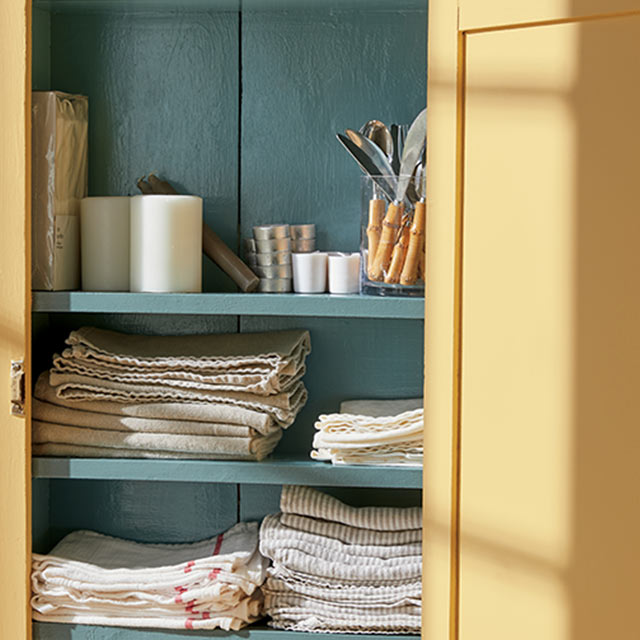 An open linen cabinet painted in Chestertown Buff HC-9 and Aegean Teal 2136-40.