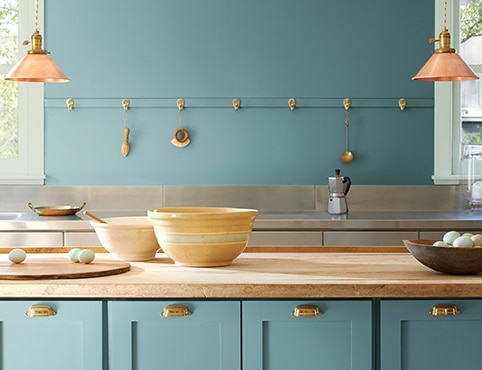 A kitchen with walls and cabinets painted in warm blue Aegean Teal 2136-40 and bowls on a butcher block countertop.