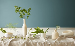 White vases and greenery on a table in front of a wall in Aegean Teal 2136-40.