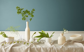 Vases blancs et végétation sur une table devant un mur peint en Vert Antique 2136-40.