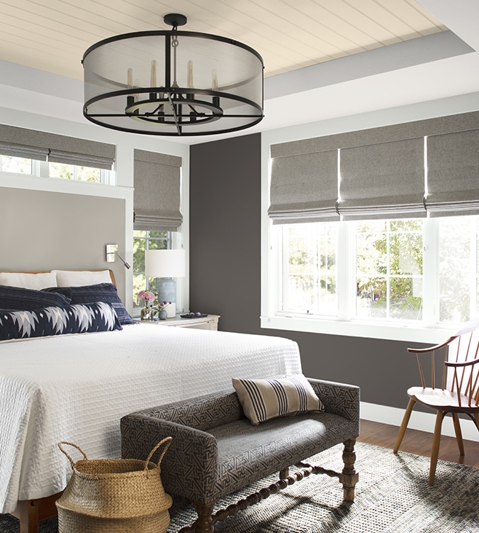 An airy bedroom with white bedding, navy and white pillows, circular chandelier, and upholstered bench.