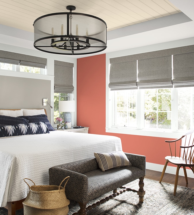 An airy bedroom with white bedding, navy and white pillows, circular chandelier, and upholstered bench.