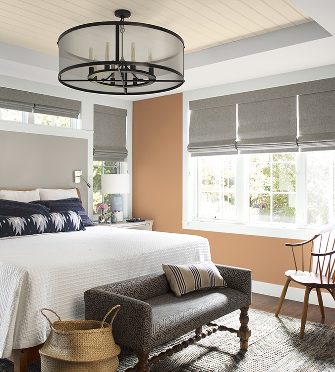 Chambre à coucher aérée avec literie blanche, oreillers et coussins bleu marine et blanc, lustre circulaire et banc rembourré