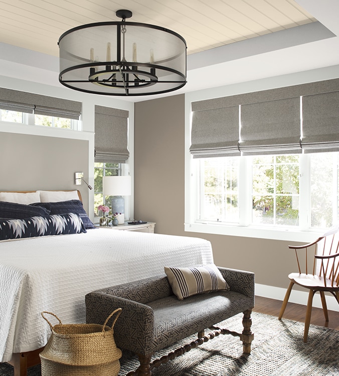An airy bedroom with white bedding, navy and white pillows, circular chandelier, and upholstered bench.