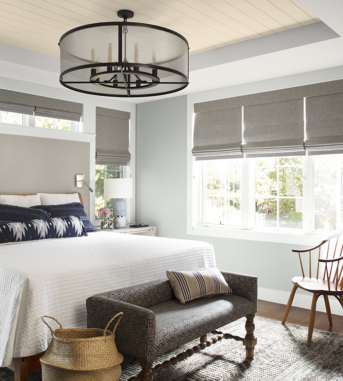 Chambre à coucher aérée avec literie blanche, oreillers et coussins bleu marine et blanc, lustre circulaire et banc rembourré