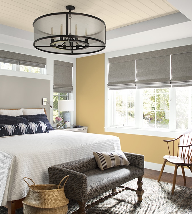 An airy bedroom with white bedding, navy and white pillows, circular chandelier, and upholstered bench.