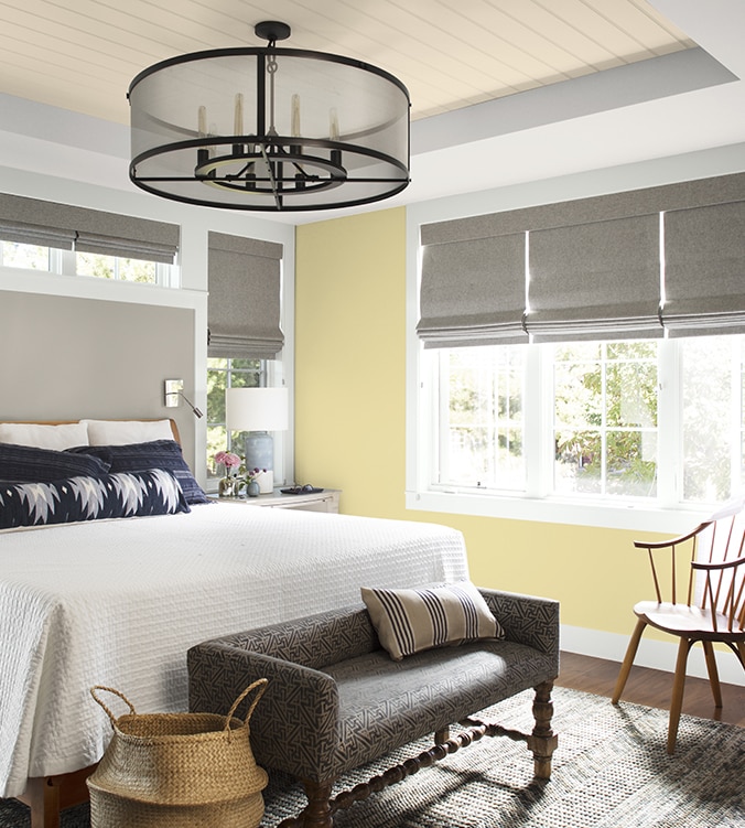 An airy bedroom with white bedding, navy and white pillows, circular chandelier, and upholstered bench.