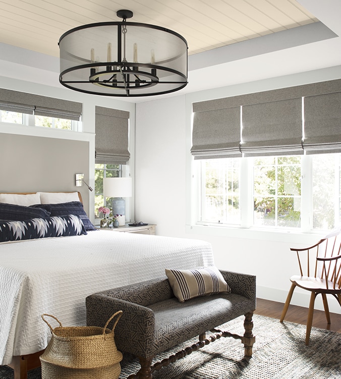 An airy bedroom with white bedding, navy and white pillows, circular chandelier, and upholstered bench.