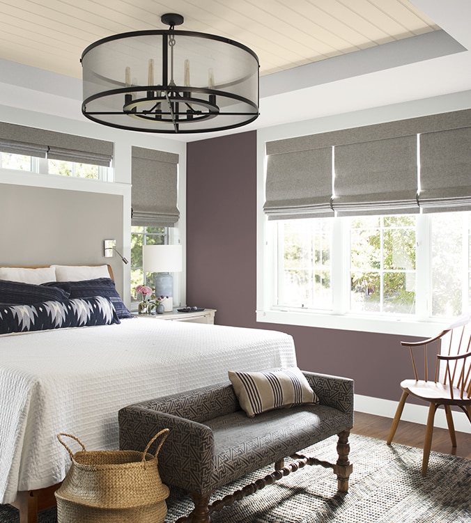 An airy bedroom with white bedding, navy and white pillows, circular chandelier, and upholstered bench.