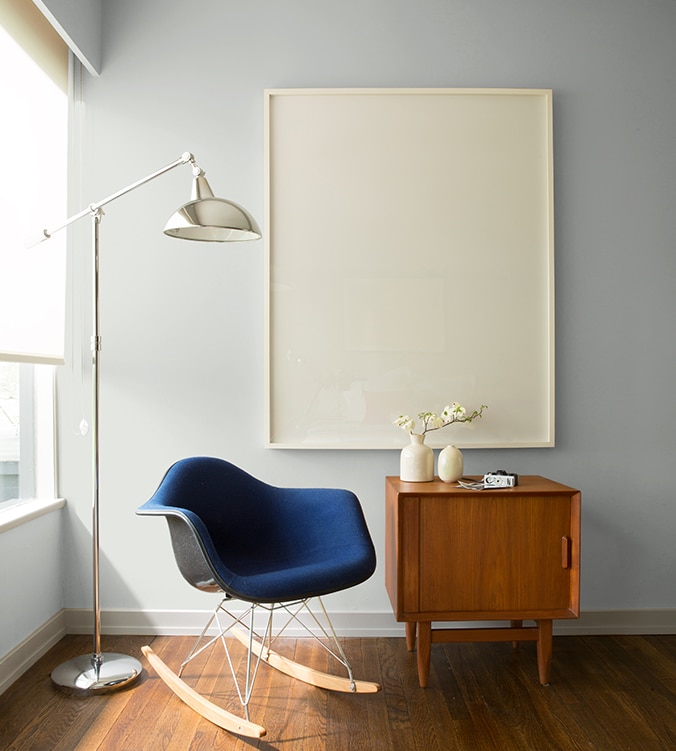 Un fauteuil berçant bleu, une table d’appui moderne des années 1950 et une lampe chromée sur pied de style contemporain agrémentent le coin de cette pièce.