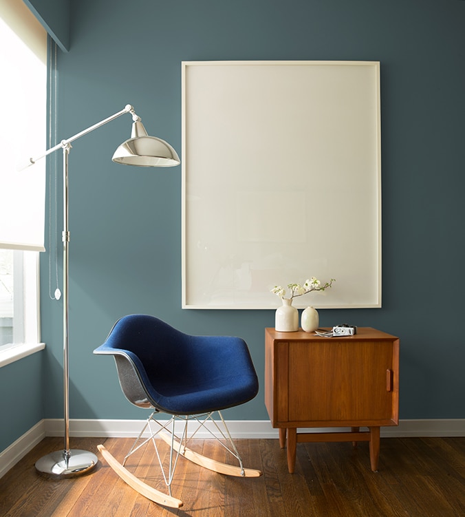 Un fauteuil berçant bleu, une table d’appui moderne des années 1950 et une lampe chromée sur pied de style contemporain agrémentent le coin de cette pièce.