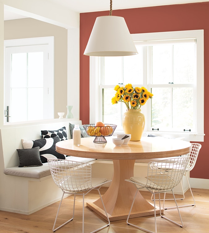 A light-filled dining area with built-in banquettes, round wood kitchen table, mesh white chairs and white pendant lamp.