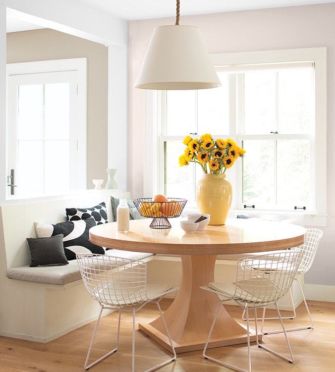 A light-filled dining area with built-in banquettes, round wood kitchen table, mesh white chairs and white pendant lamp.