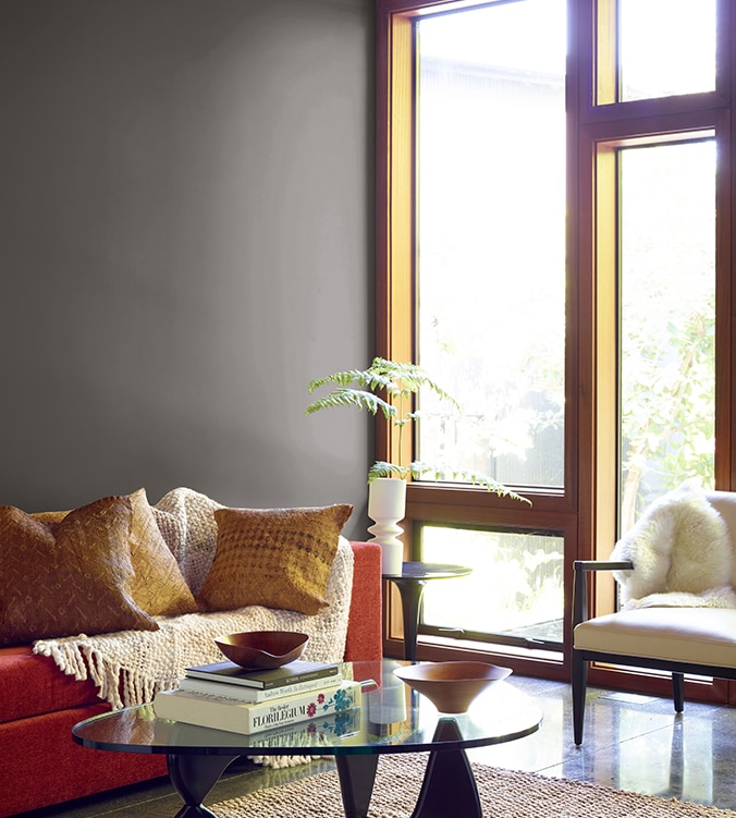 A contemporary den with floor-to-ceiling-windows, modern glass coffee table, and orange couch with cream colour throw.