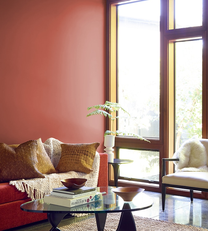 A contemporary den with floor-to-ceiling-windows, modern glass coffee table, and orange couch with cream colour throw.