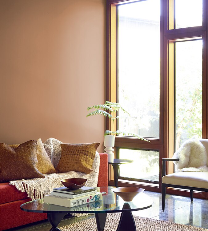 A contemporary den with floor-to-ceiling-windows, modern glass coffee table, and orange couch with cream colour throw.