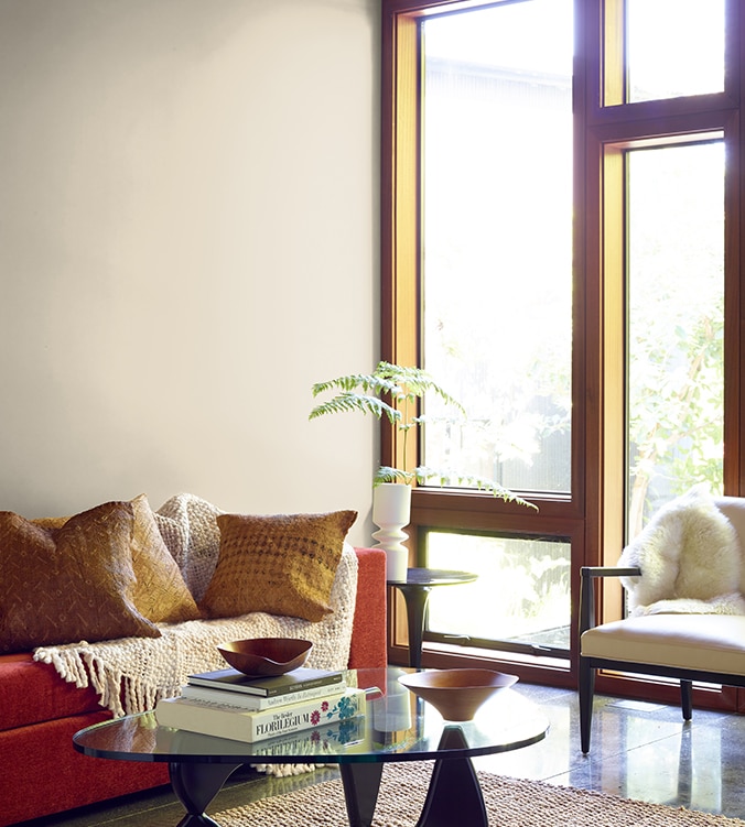 A contemporary den with floor-to-ceiling-windows, modern glass coffee table, and orange couch with cream colour throw.