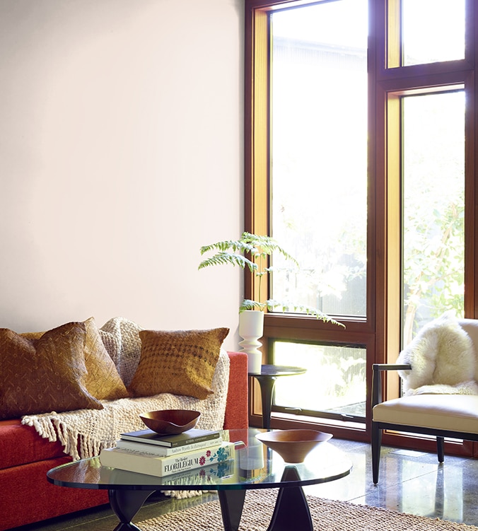 A contemporary den with floor-to-ceiling-windows, modern glass coffee table, and orange couch with cream colour throw.