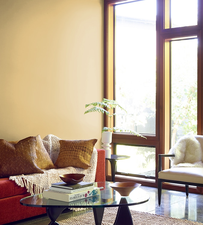 A contemporary den with floor-to-ceiling-windows, modern glass coffee table, and orange couch with cream colour throw.