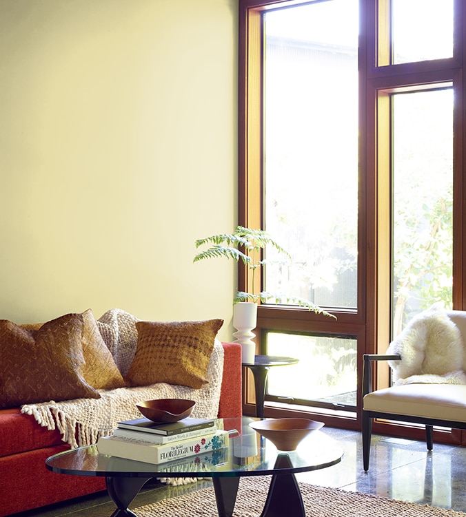 Boudoir contemporain avec fenêtres pleine longueur, table basse en verre de style moderne et canapé orangé avec jeté de couleur crème.