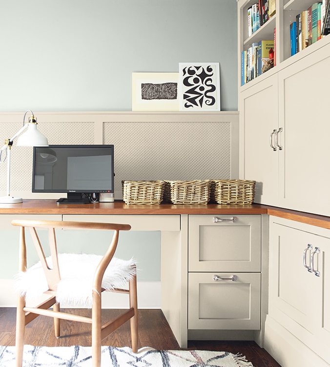 Coin-bureau avec table de travail encastrée, armoires et étagères, chaise en bois doré et lampe de bureau blanche.