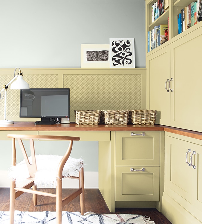 Coin-bureau avec table de travail encastrée, armoires et étagères, chaise en bois doré et lampe de bureau blanche.