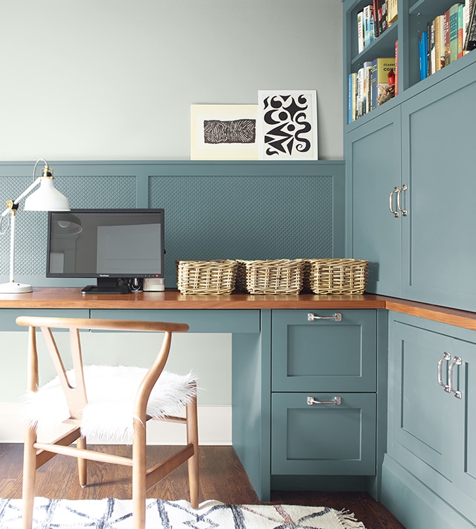 Coin-bureau avec table de travail encastrée, armoires et étagères, chaise en bois doré et lampe de bureau blanche.