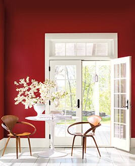 A rich red sitting room is flooded with light through several white French doors. 