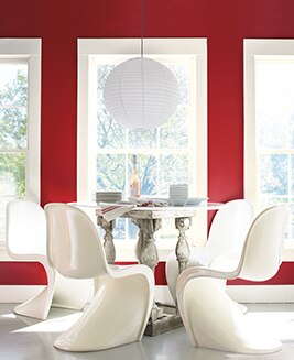 An intimate dining room with four white tulip chairs offers a view through large windows framed in white against a striking red dining room wall.