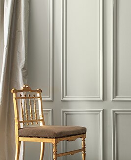 Le mur gris et les rideaux en soie de couleur crème mettent en scène une chaise dorée élégante.