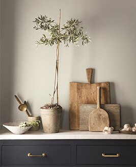 Tiroirs marine et comptoir de marbre sur lequel reposent plusieurs éléments végétaux et outils de jardinage, le tout soutenu par un mur gris. 
